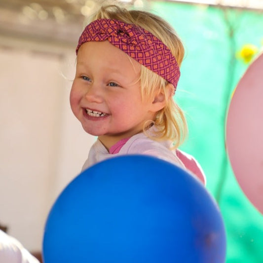 petite fille blonde avec bandeau de tête rose à nœud croisé et un ballon bleu 