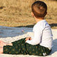 un petit garçon assis sur une couverture avec un pantalon imprimé shweshwe vert avec une fleur dans les mains 